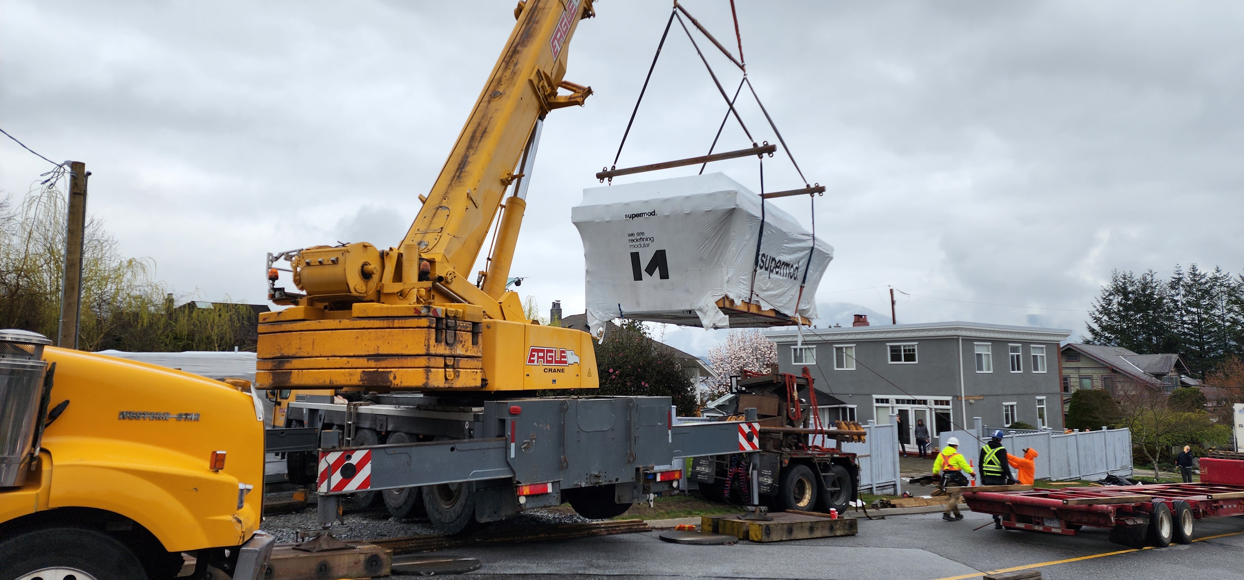 A crane lifting a completed modular building module into place at a Deep Cove, BC building site